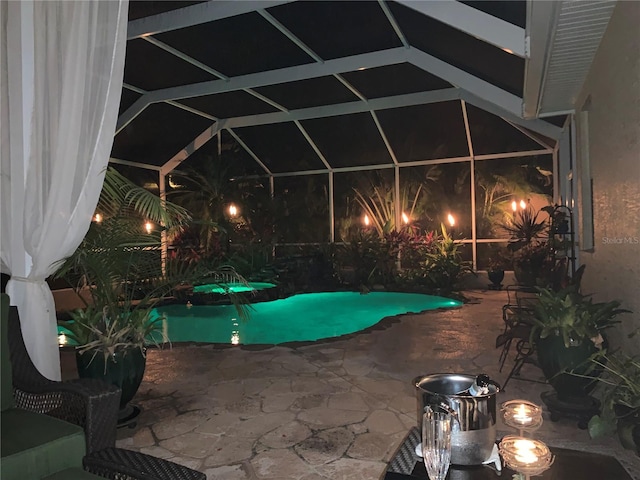 pool at night featuring glass enclosure and a patio area