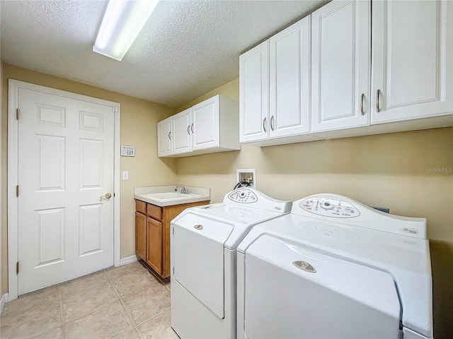 washroom with light tile patterned floors, cabinet space, washing machine and dryer, a sink, and a textured ceiling