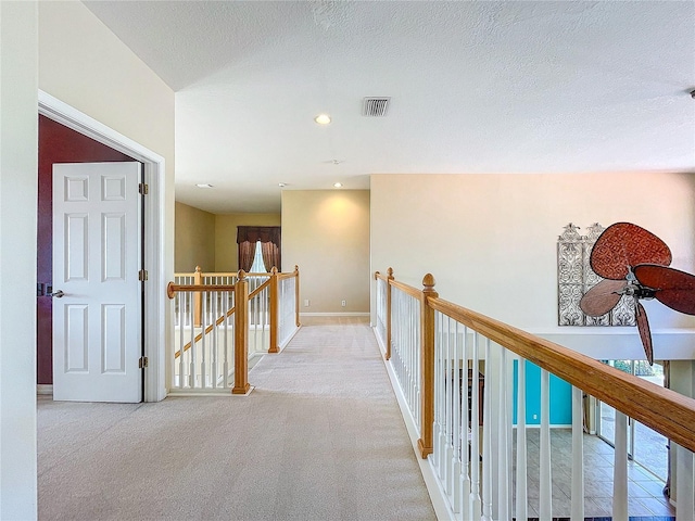 corridor with light colored carpet, visible vents, a textured ceiling, an upstairs landing, and baseboards