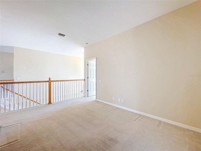 spare room featuring light colored carpet, visible vents, a textured ceiling, and baseboards