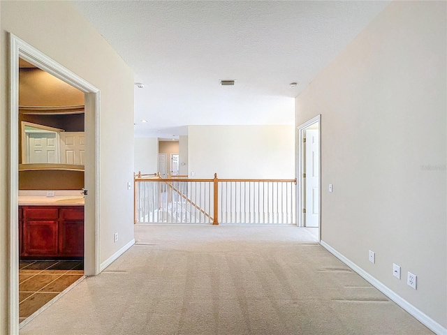 spare room with carpet floors, visible vents, a textured ceiling, and baseboards