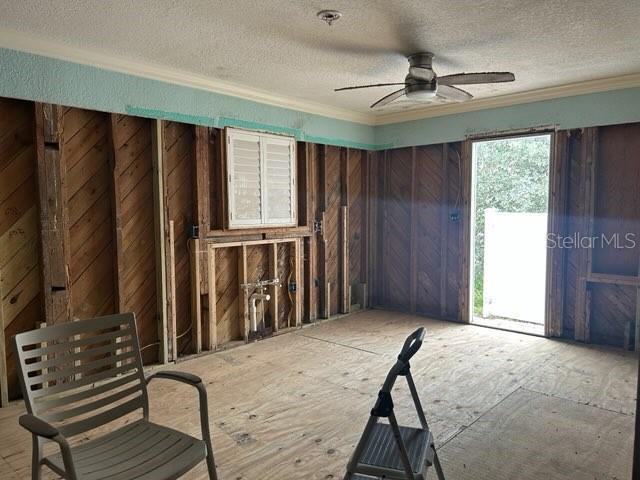 interior space featuring wood walls, a textured ceiling, a ceiling fan, and crown molding