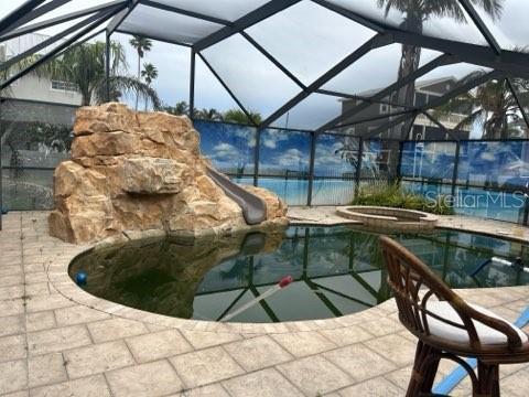 outdoor pool featuring an in ground hot tub, a water slide, a patio, and a lanai