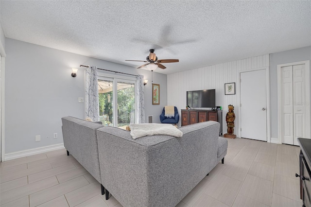 living area with a ceiling fan, a textured ceiling, and baseboards