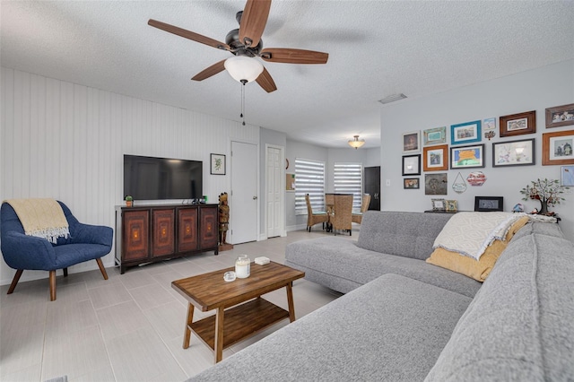 living room with a textured ceiling, ceiling fan, light tile patterned flooring, and visible vents