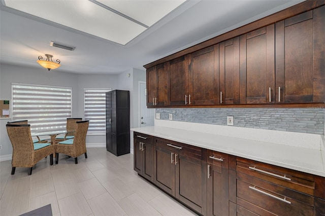 kitchen featuring dark brown cabinetry, baseboards, visible vents, light countertops, and backsplash