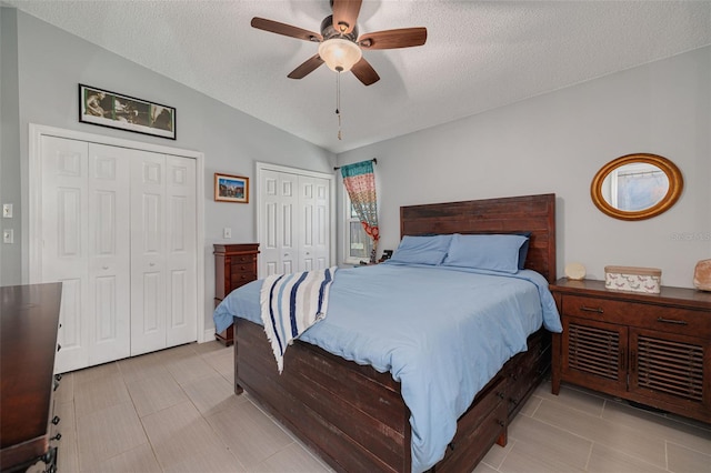 bedroom featuring vaulted ceiling, ceiling fan, a textured ceiling, and multiple closets