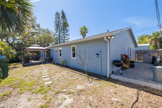 rear view of house featuring stucco siding, a gazebo, a patio area, fence, and cooling unit