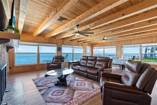 living room with wood walls, a water view, wood ceiling, a brick fireplace, and beamed ceiling