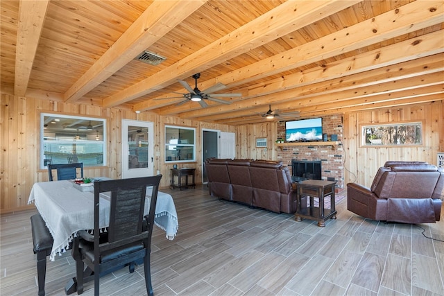 living area featuring wood walls, a fireplace, visible vents, and beamed ceiling