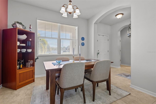 dining area featuring arched walkways, light tile patterned flooring, a notable chandelier, and baseboards