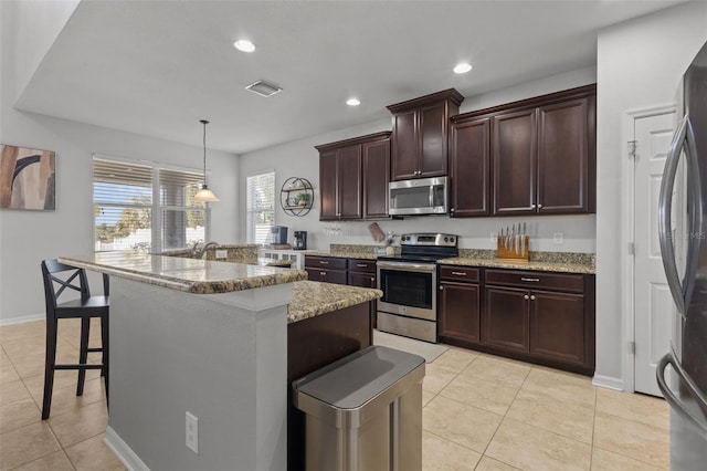 kitchen with light tile patterned floors, appliances with stainless steel finishes, visible vents, and a kitchen breakfast bar