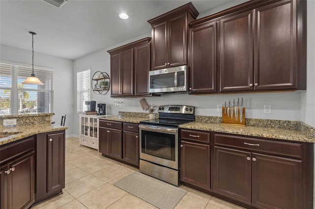 kitchen featuring light tile patterned flooring, dark brown cabinets, appliances with stainless steel finishes, hanging light fixtures, and light stone countertops