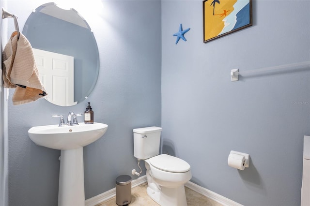 half bathroom featuring baseboards, a sink, toilet, and tile patterned floors