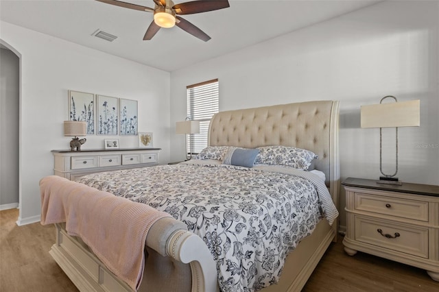 bedroom featuring arched walkways, visible vents, ceiling fan, wood finished floors, and baseboards