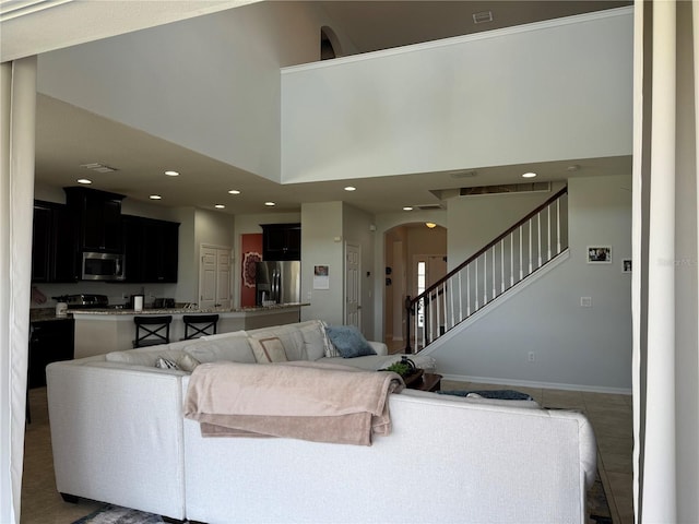 living room featuring arched walkways, recessed lighting, a towering ceiling, baseboards, and stairs