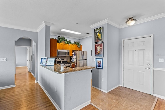 kitchen with arched walkways, stainless steel appliances, a peninsula, and crown molding