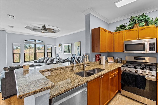 kitchen featuring light stone counters, crown molding, appliances with stainless steel finishes, open floor plan, and a sink