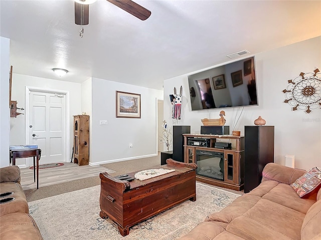 carpeted living area with a ceiling fan, a glass covered fireplace, visible vents, and baseboards