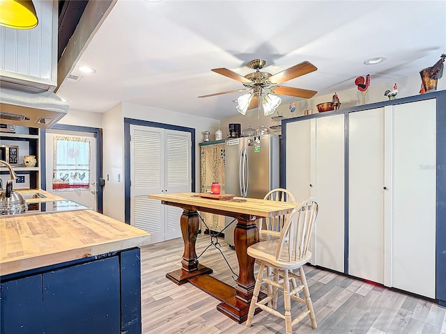 kitchen with blue cabinetry, freestanding refrigerator, wood counters, and light wood finished floors