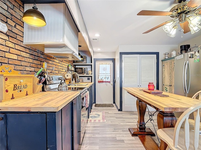 kitchen featuring appliances with stainless steel finishes, light wood-type flooring, wood counters, and brick wall