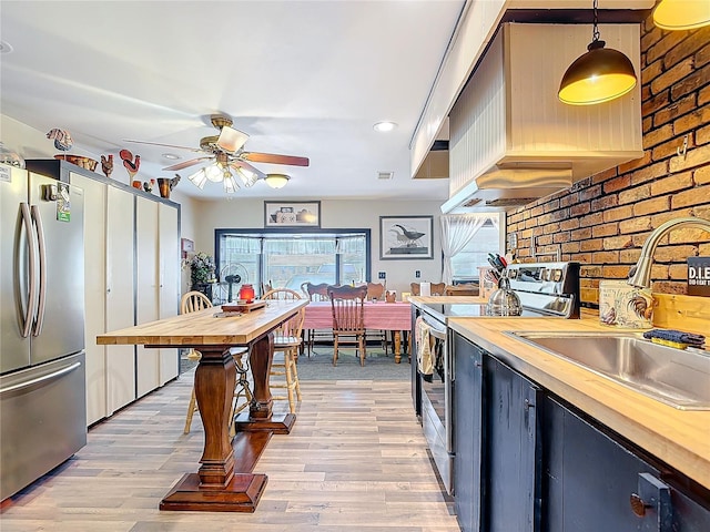 kitchen featuring light wood-type flooring, butcher block counters, stainless steel appliances, and a sink