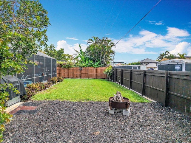 view of yard featuring a lanai, a fenced backyard, and a fire pit