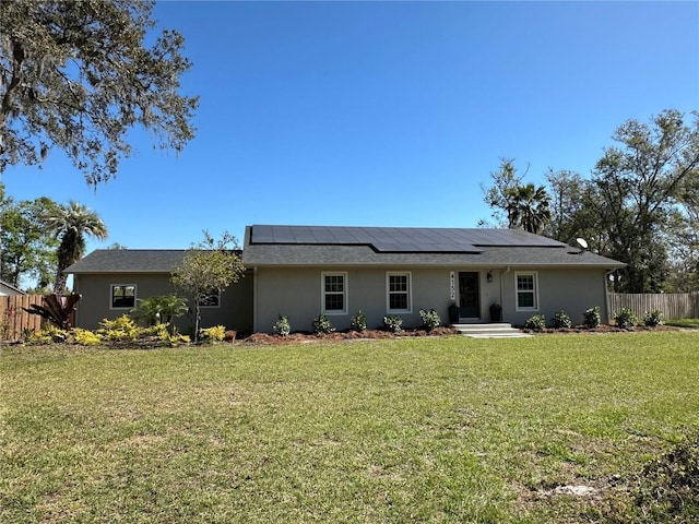 view of front of property with roof mounted solar panels, fence, a front lawn, and stucco siding