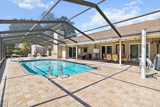 outdoor pool featuring glass enclosure, a ceiling fan, and a patio