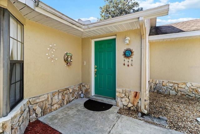 property entrance with stone siding, roof with shingles, and stucco siding