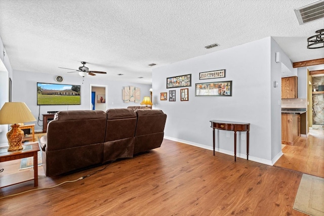 living area featuring visible vents, ceiling fan, a textured ceiling, and wood finished floors