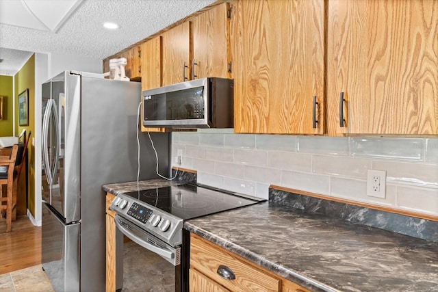 kitchen with stainless steel appliances, dark countertops, a textured ceiling, and tasteful backsplash