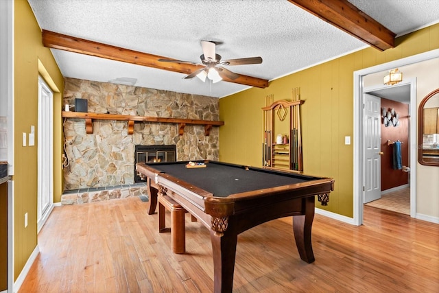 rec room with light wood-style floors, beam ceiling, a fireplace, and a textured ceiling