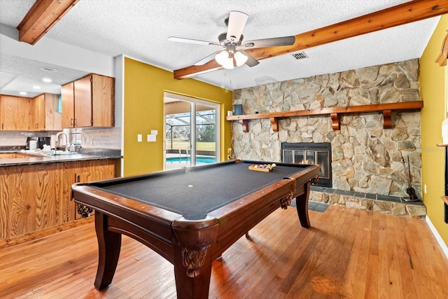 recreation room with a textured ceiling, light wood finished floors, a fireplace, and beam ceiling