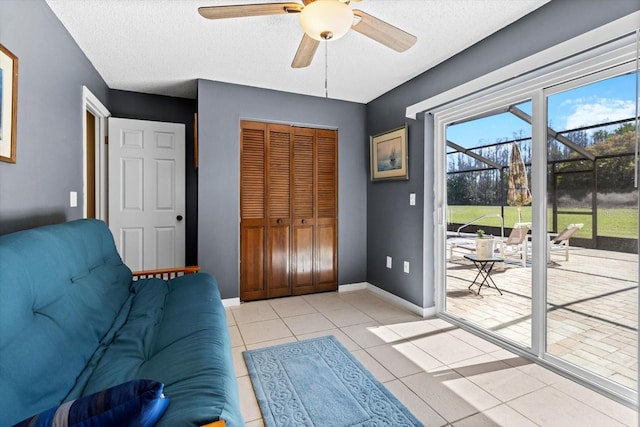 interior space with a ceiling fan, light tile patterned flooring, a textured ceiling, and baseboards