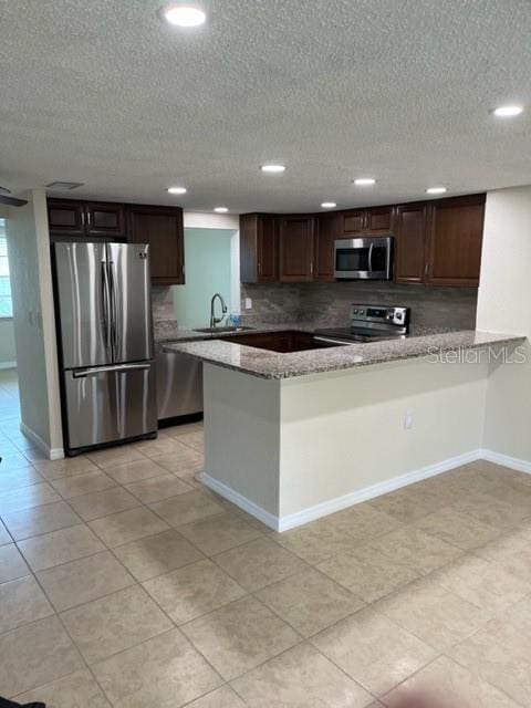 kitchen featuring stainless steel appliances, backsplash, a sink, dark brown cabinetry, and baseboards