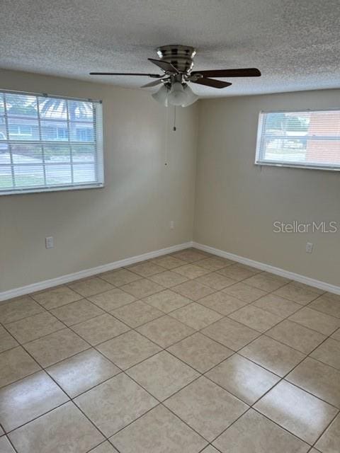 unfurnished room featuring light tile patterned flooring, ceiling fan, a textured ceiling, and baseboards