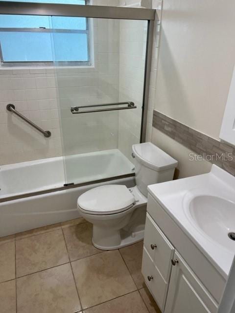 full bath with combined bath / shower with glass door, vanity, toilet, and tile patterned floors