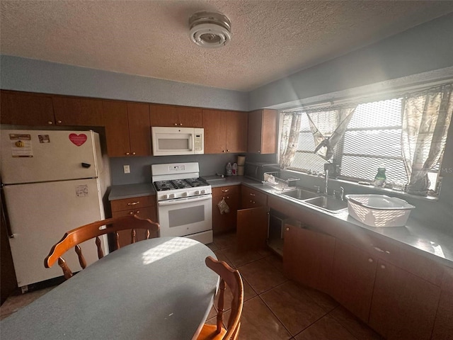 kitchen with brown cabinetry, a sink, a textured ceiling, white appliances, and dark tile patterned floors