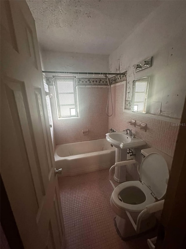 bathroom with plenty of natural light, a textured ceiling, toilet, and tile patterned floors