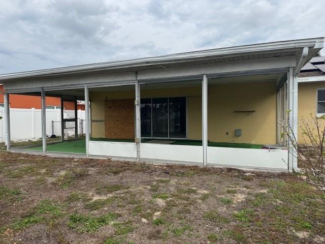 rear view of house with a sunroom, fence, and stucco siding