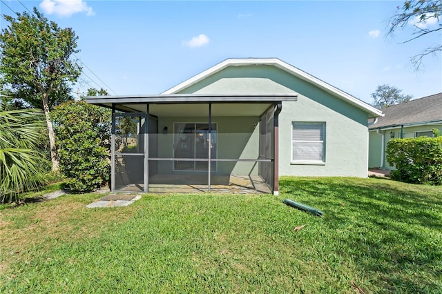 back of property featuring a sunroom, a yard, and stucco siding