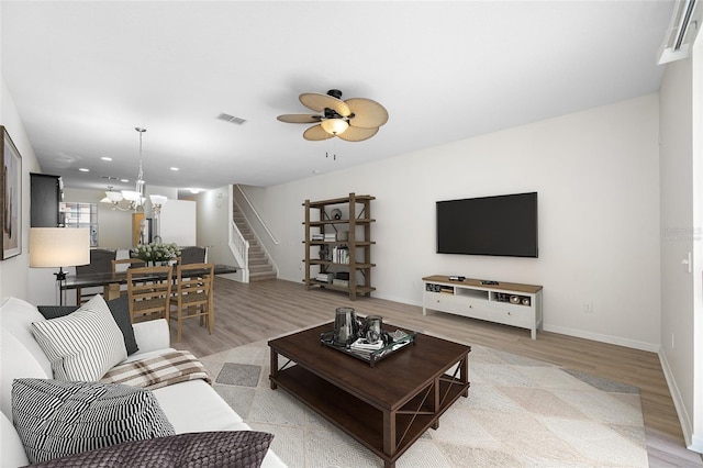 living room featuring stairway, light wood-style flooring, visible vents, and ceiling fan with notable chandelier