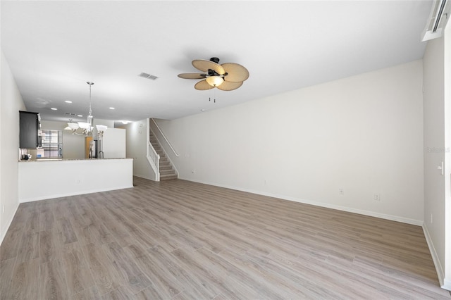 unfurnished living room with light wood-style flooring, ceiling fan with notable chandelier, visible vents, baseboards, and stairway