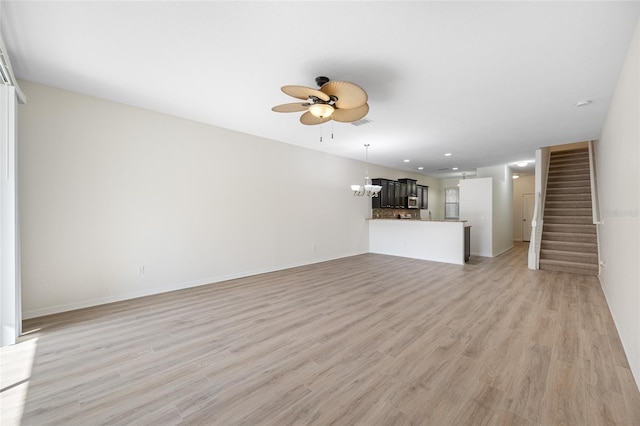 unfurnished living room with ceiling fan with notable chandelier, visible vents, baseboards, stairs, and light wood-type flooring