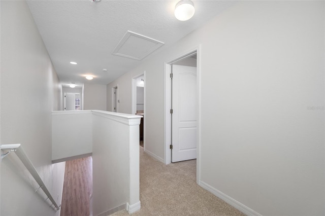 hallway with a textured ceiling, light carpet, an upstairs landing, baseboards, and attic access