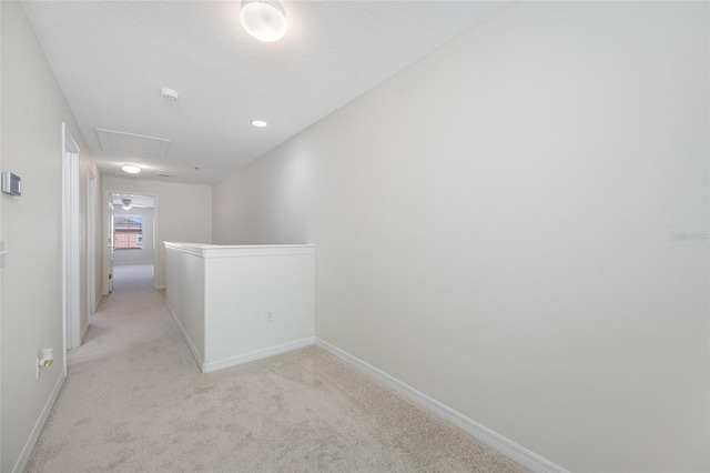 corridor featuring an upstairs landing, baseboards, a textured ceiling, and light colored carpet