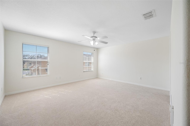 spare room with visible vents, ceiling fan, light carpet, and baseboards