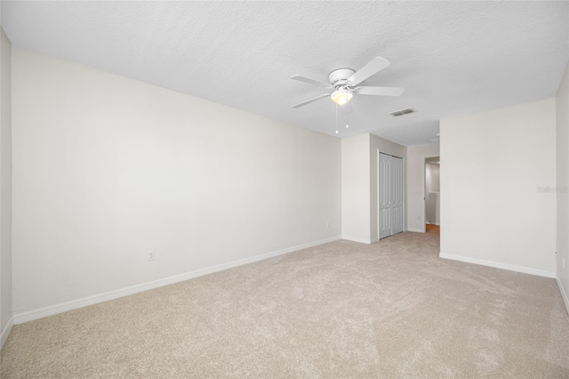 unfurnished room with a textured ceiling, ceiling fan, light colored carpet, visible vents, and baseboards