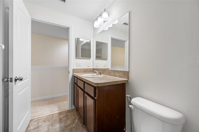 bathroom with visible vents, a textured wall, toilet, vanity, and baseboards